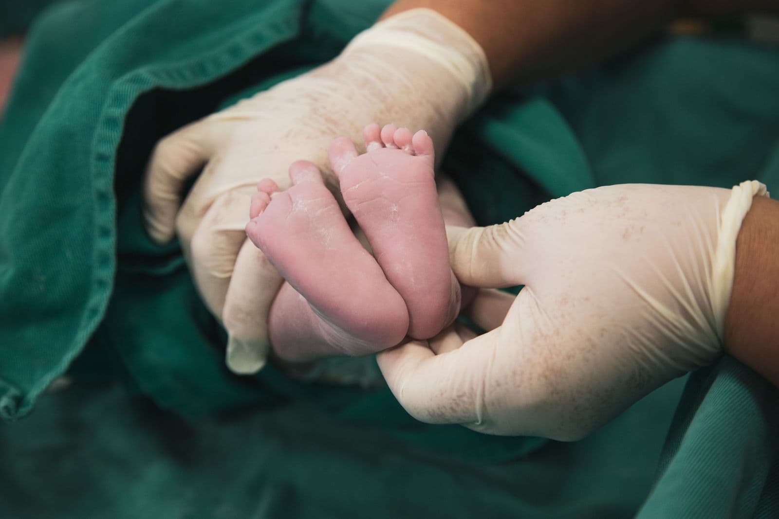 Mãos com luvas cirúrgicas segurando os pés de um recém-nascido na sala de parto
